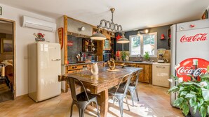 Une cuisine avec une table en bois, des chaises en métal, un r éfrigérateur et une enseigne Coca-Cola.