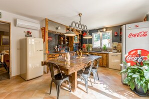 A kitchen with a wooden table, metal chairs, a refrigerator, and a Coca-Cola sign. - Charming Provence Villa with Pool, Wi-Fi, and Air Conditioning (Rochegude)