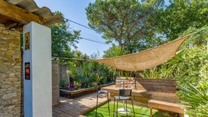 Une terrasse en bois avec un hamac, un barbecue et un espace détente avec des chaises.