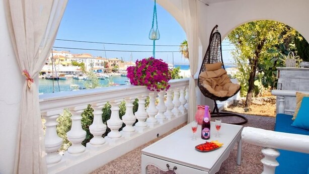 Een balkon met uitzicht op zee, een hangstoel, een tafel met een drankje en een bank.