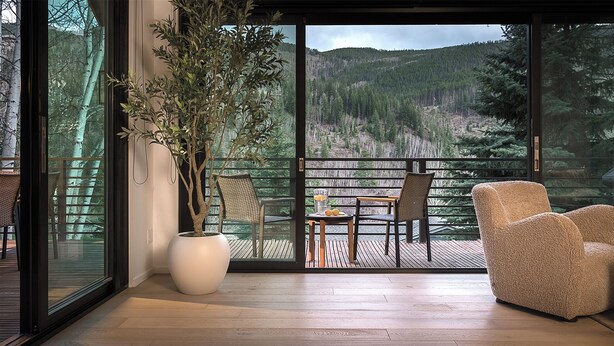 A room with a large sliding glass door leading to a deck with a view of a forested mountain. - Sleek, Light-Filled Alpine Escape | Hot Tub, Wine Room | Axiom Retreat (Vail)