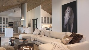 A modern living room with a sofa, coffee table, and a painting of a horse. - Sleek, Light-Filled Alpine Escape | Hot Tub, Wine Room | Axiom Retreat (Vail)