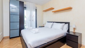 Un dormitorio moderno con cama, mesitas de noche, un armario y vistas a través de un ventanal.
