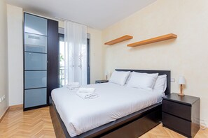 Ein modernes Schlafzimmer mit Bett, Nachttischen, einem Kleiderschrank und Blick durch eine Glastür.