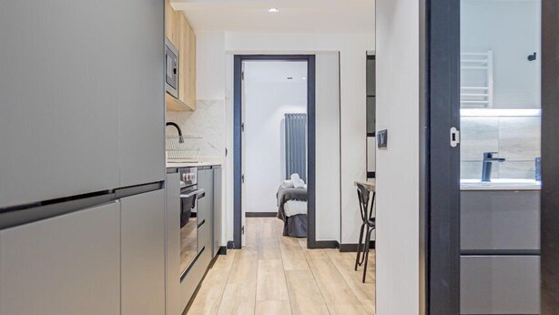 A modern kitchen with grey cabinets, a wooden floor, and a view into the living area. - GuestReady - Modern apartment in the city centre (Madrid)