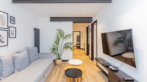 A modern living room with a sofa, a small table, a potted plant, and a flat-screen TV mounted on the wall. - GuestReady - Modern apartment in the city centre (Madrid)