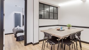 A modern room with a wooden dining table, four chairs, a potted plant, and a large window. - GuestReady - Modern apartment in the city centre (Madrid)