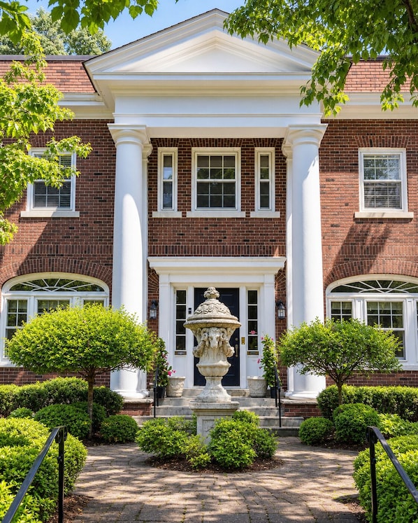 A brick building with a central entrance, flanked by columns, and a decorative urn in front.