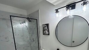 A bathroom with a glass shower enclosure, a toilet, a sink with a mirror, and a small potted plant.