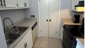 A compact kitchen with white cabinets, a double door, a sink, a dishwasher, and a stove.