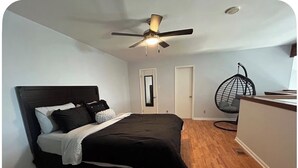 A bedroom with a bed, a ceiling fan, a hanging chair, and a door.
