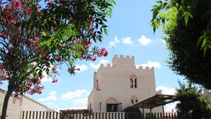 A castle-like building with a covered patio, surrounded by a fence and greenery.