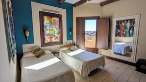 A room with two beds, a large window with a view, and a stained glass window.