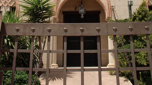 A building with a large arched entrance labeled 'La Alcazaba,' featuring a castle-like facade with battlements and a clear blue sky in the background.