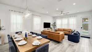 Ein modernes Wohnzimmer mit einem Holzesstisch, gedeckt für vier Personen, einer Couch, einem Fernseher und einem Deckenventilator.