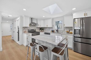 Una cocina moderna con armarios blancos, una isla grande, electrodomésticos de acero inoxidable y un tragaluz.