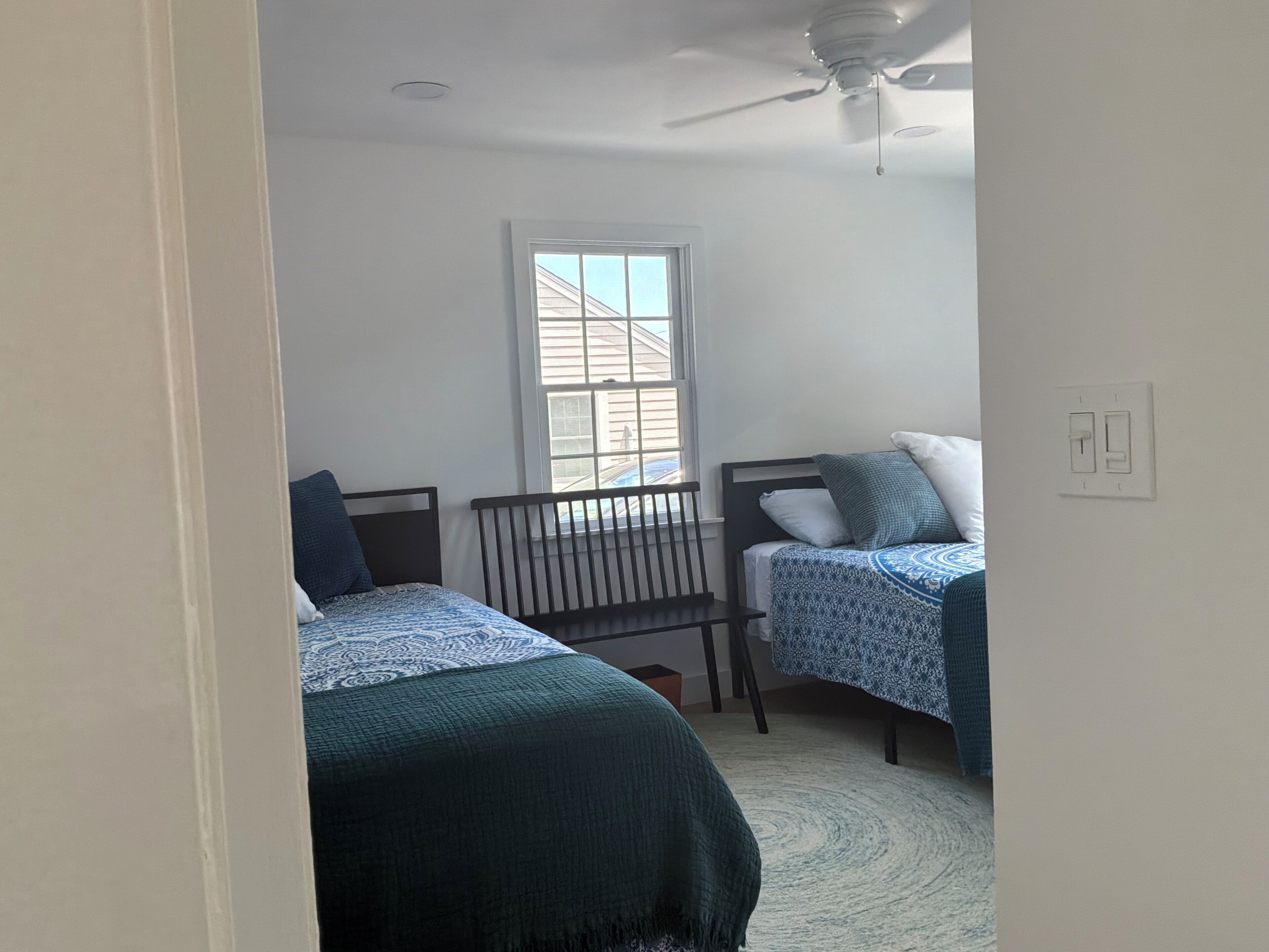 A bedroom with two beds, a window, a ceiling fan, and a light switch.