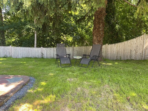 Un jardin avec une clôture en bois, deux chaises de jardin et une petite table ronde.