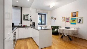 A modern kitchen with white cabinetry, a dining area with a round table and chairs, and artwork on the walls. - Comfortable Apartment Steps from the Red Metro Line (Milano)