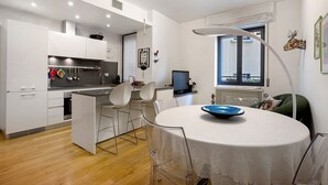 A modern kitchen with white cabinets, a dining area with a round table, and a large window with a view. - Comfortable Apartment Steps from the Red Metro Line (Milano)