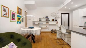 A modern kitchen with white cabinets, a dining area with a round table and chairs, and a green sofa with a floral cushion. - Comfortable Apartment Steps from the Red Metro Line (Milano)