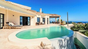 Ett hus med en swimmingpool, utomhusmöbler och utsikt över havet.