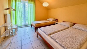 A room with two beds, a desk, a hanging light fixture, and a view through a window with green curtains. - Holiday Home 'Whirlpool Kicker Sauna Gruppenhaus' with Mountain View, Private Terrace & Wi-Fi (Kemmenau)