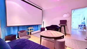 Ein Raum mit Projektionsleinwand, einem runden Tisch und zwei Stühlen.