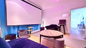 A room with a projector screen, a round table, and two chairs.