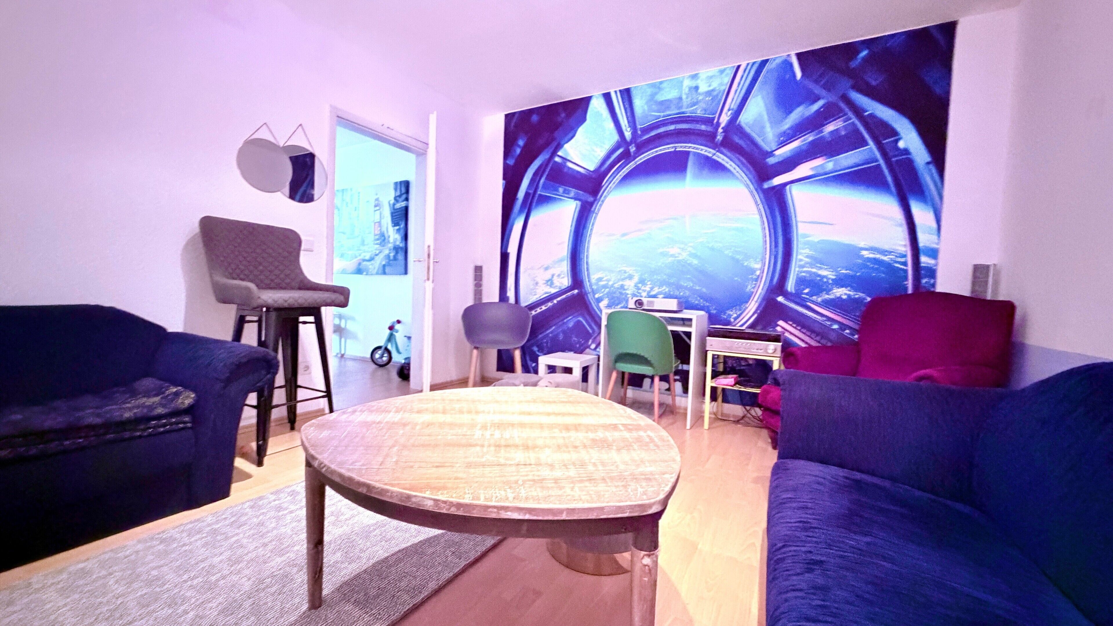 A living room with a round table, two sofas, a green chair, and a wall mural.