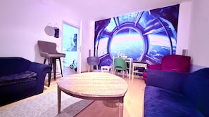 Ein Wohnzimmer mit einem runden Tisch, zwei Sofas, einem grünen Sessel und einer Wandmalerei.