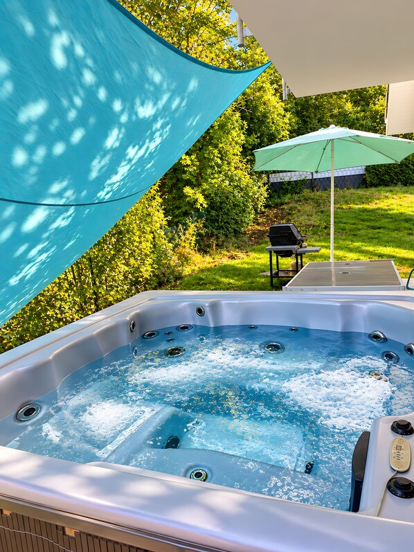 A hot tub with a control panel, surrounded by a grassy area and trees.
