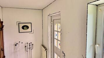 Un couloir étroit avec un radiateur, un petit tabouret blanc et une porte ornée de vitraux.