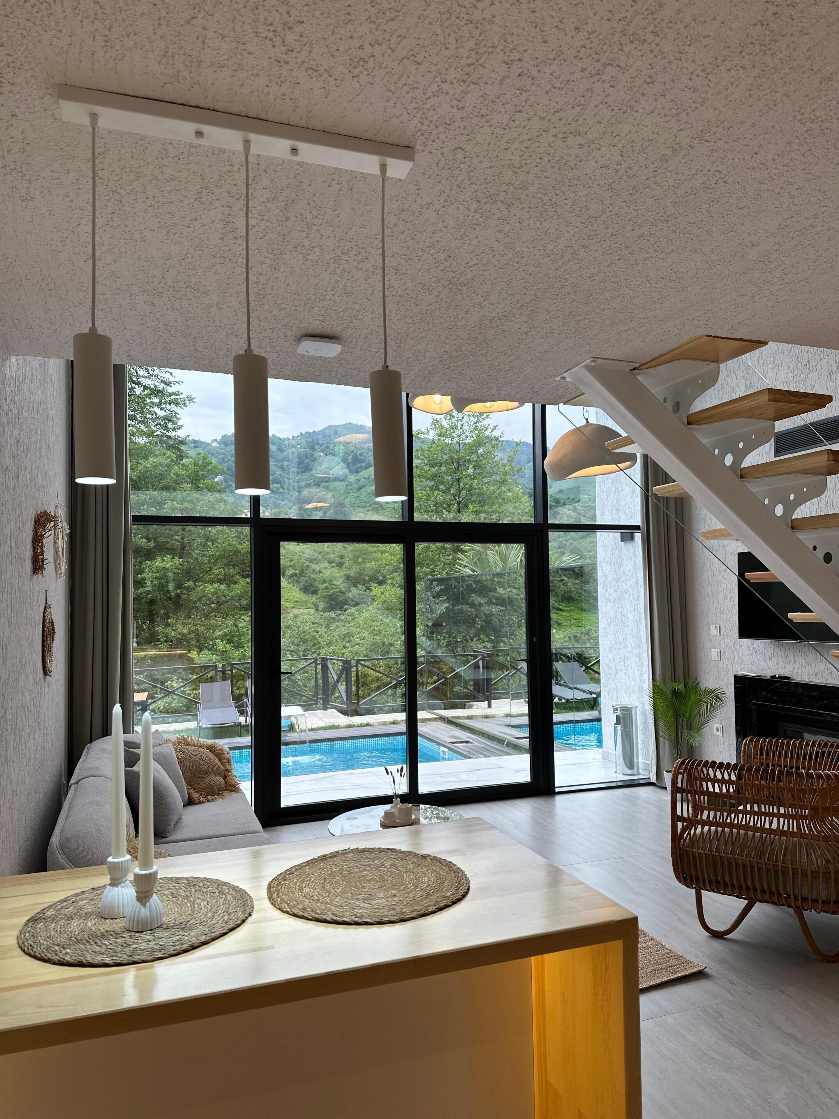 A modern living room with a large window, a pool view, and a staircase.