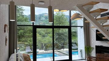 A modern living room with a large window, a pool view, and a staircase.