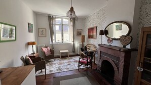 A cozy room with a fireplace, a wooden chair, a small table, and a patterned rug. - Le logis des ais. Historic townhouse in city center (La Charité-sur-Loire)