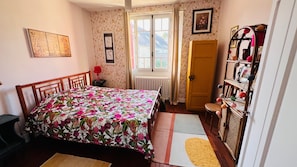 A bedroom with a bed, a radiator, a window, a door, and a dresser. - Le logis des ais – Historic Townhouse in City Center (La Charité-sur-Loire)