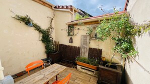 A wooden deck with a table and chairs, potted plants, a wooden fence, and a wall with a window and a door. - Le logis des ais. Historic townhouse in city center (La Charité-sur-Loire)