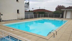 A rectangular swimming pool with a white metal ladder and a white fence surrounding it.