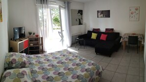 A room with a bed, a black sofa, a small table, a TV, and a window with curtains.