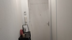 A hallway with a closed door, a small desk with a telephone and a framed certificate, and a wall-mounted thermostat.