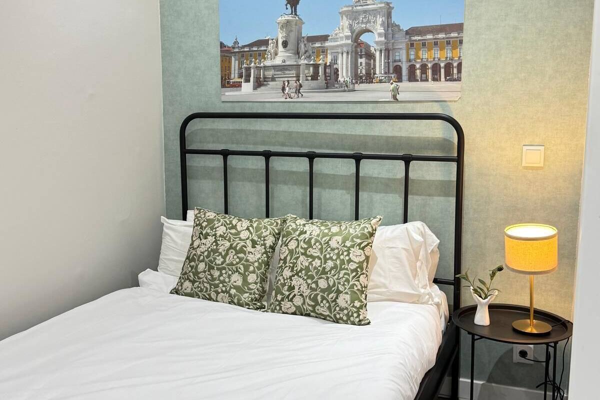 Habitación de hotel con cama, mesita de noche con lámpara, cuadro colgado en la pared de un edificio histórico y ventana con vista al edificio.