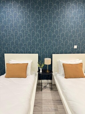 A hotel room with two beds, a small table with a lamp, and a decorative wall pattern.
