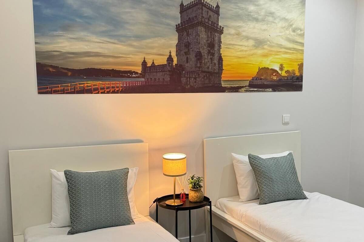 Habitación de hotel con dos camas, una mesita de noche con lámpara y un cuadro grande de un edificio histórico.