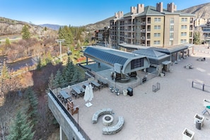 A hotel with a covered outdoor seating area, a circular stone feature, and a view of a river and mountains. - Prime Avon Location | Riverfront + Walk Everywhere (Avon)