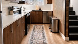 Eine moderne Küche mit Holzschränken, Edelstahlgeräten und einem gemusterten Teppich.