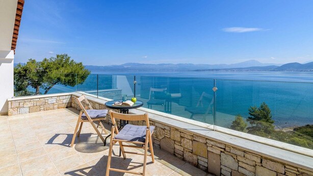 A balcony with a clear view of a large body of water, a stone wall, and two wooden chairs.