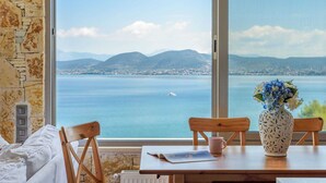A room with a large window, a wooden table, a vase with flowers, and a view of a lake and mountains.