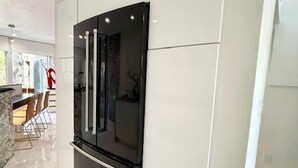 Eine moderne Küche mit einem schwarzen Kühlschrank, weißen Schränken und einem Essbereich mit Stühlen.