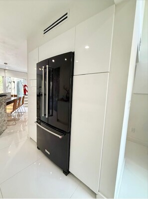 Eine moderne Küche mit einem schwarzen Kühlschrank, weißen Schränken und einem Essbereich mit Stühlen.